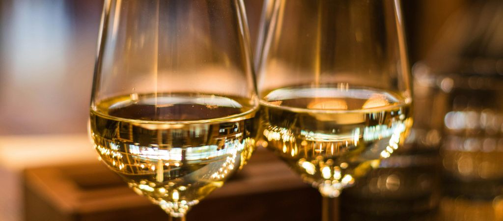 Two wine glasses with white wine site on a wooden table.